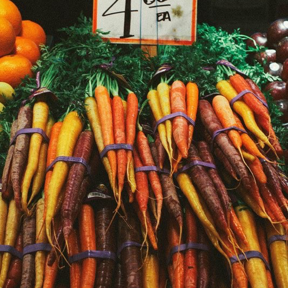 Bundles of colorful carrots, including orange, yellow, and purple varieties, displayed at a market.