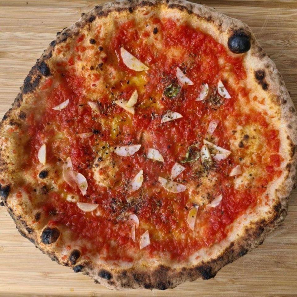 Bloom pizzeria's marinara pizza with tomato sauce, garlic, and oregano on a wooden board.