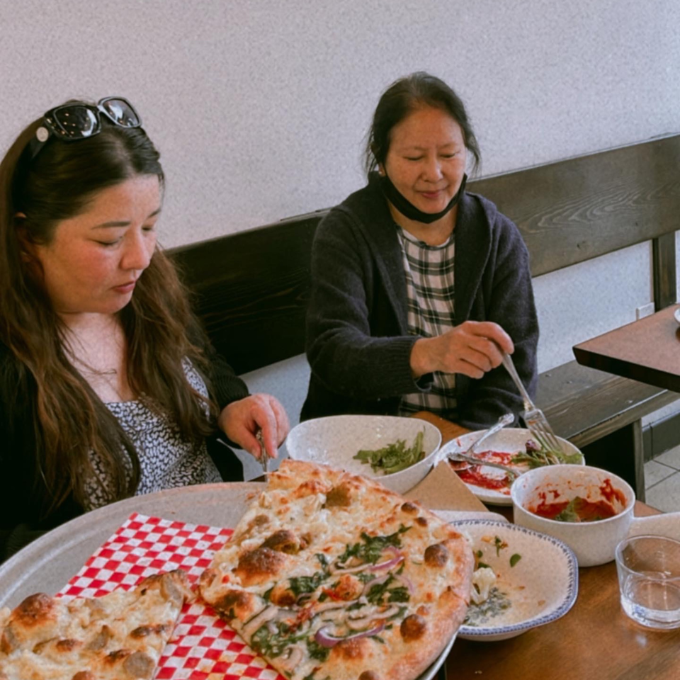 Two women enjoying pizza and salads at Bloom Pizzeria, with a large pizza in the foreground.