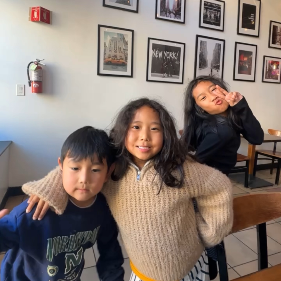 Three children posing happily inside Bloom pizzeria, with New York-themed pictures on the wall.