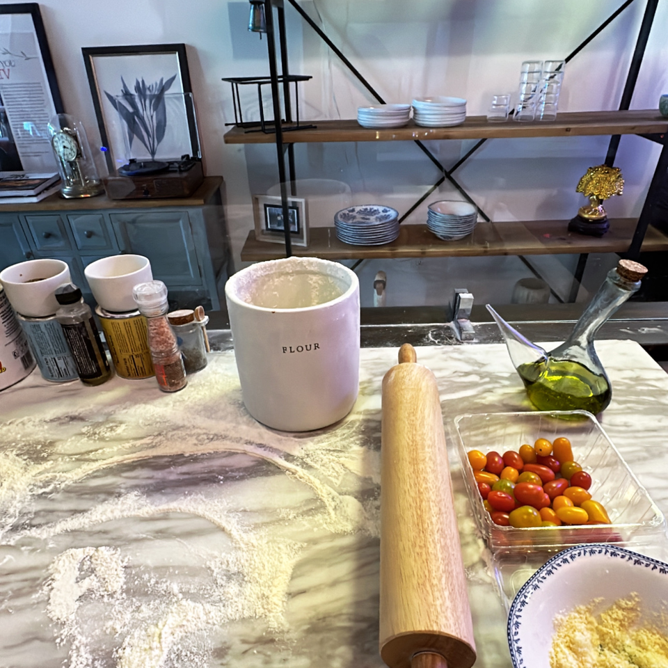 Flour-dusted marble counter with rolling pin, tomatoes, olive oil, and spices, ready for pizza making.