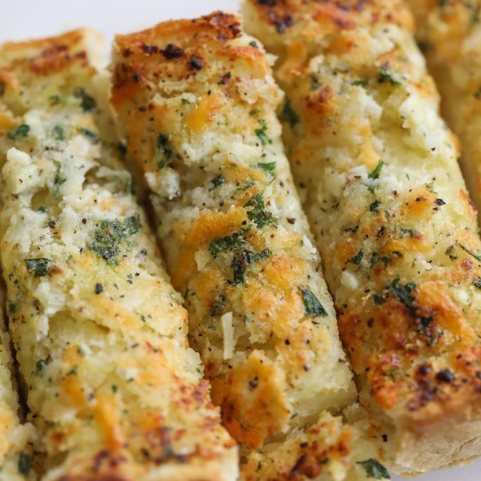 Close-up of Bloom pizzeria's golden-brown garlic breadsticks, topped with melted cheese and green herbs.