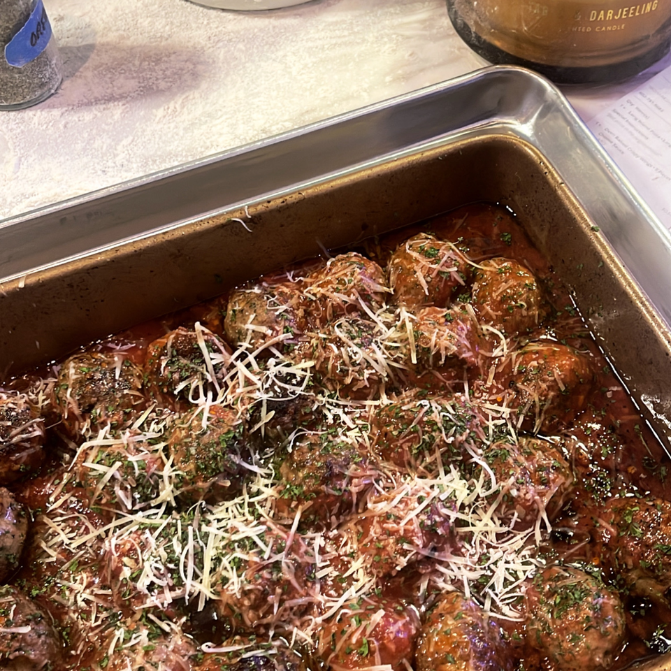 A pan of Bloom pizzeria's meatballs in marinara sauce, topped with shredded cheese and herbs.