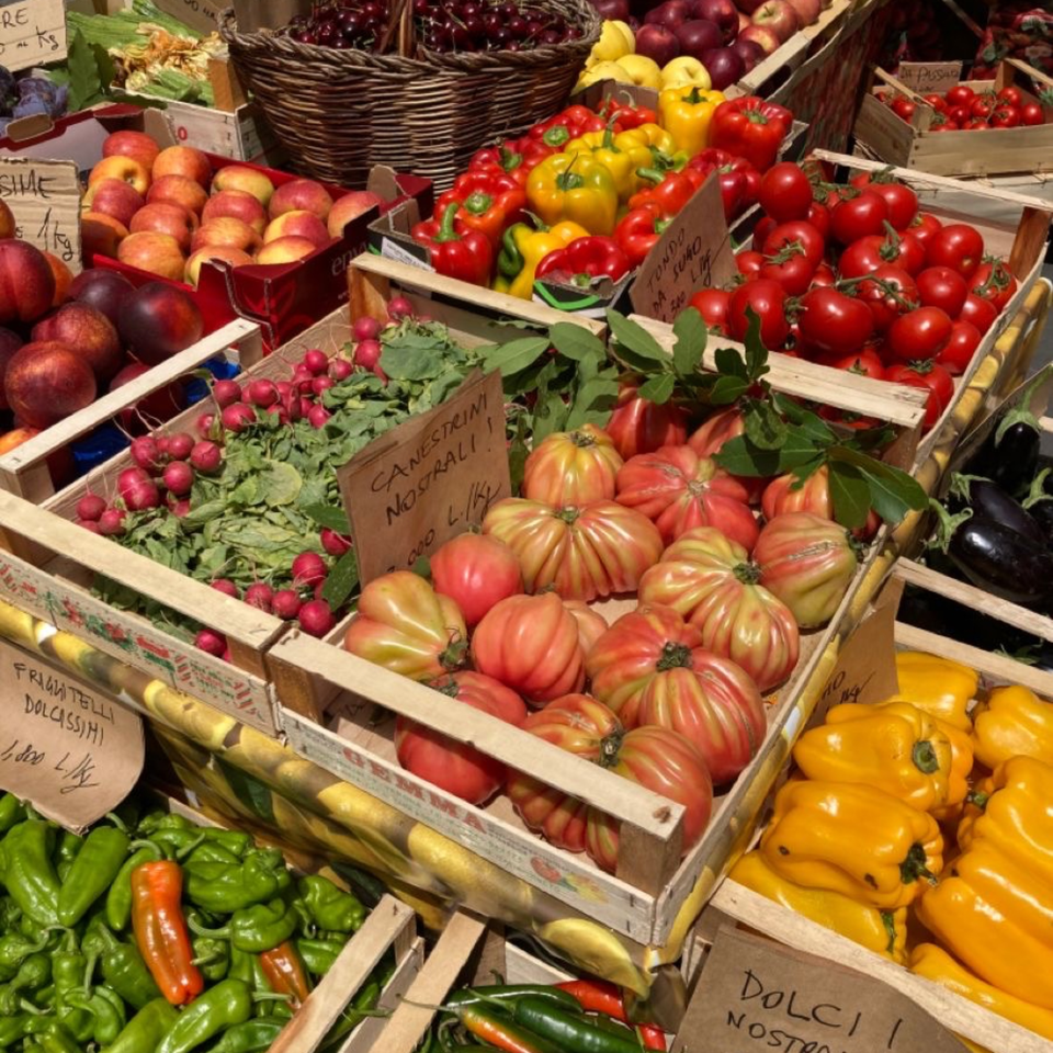 Wooden crates overflowing with fresh, colorful produce like tomatoes, peppers, radishes, and apples at a market.
