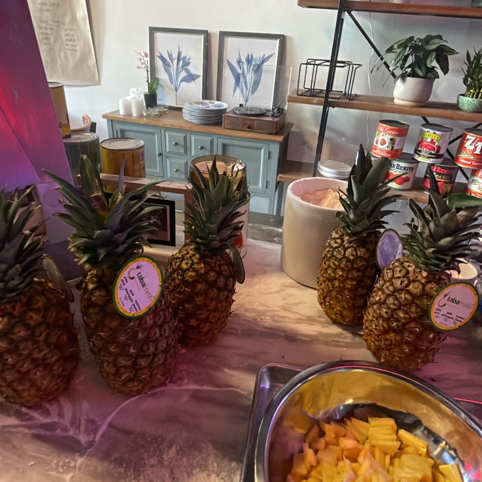 Whole pineapples and a bowl of chopped pineapple on a counter, with canned goods in the background.