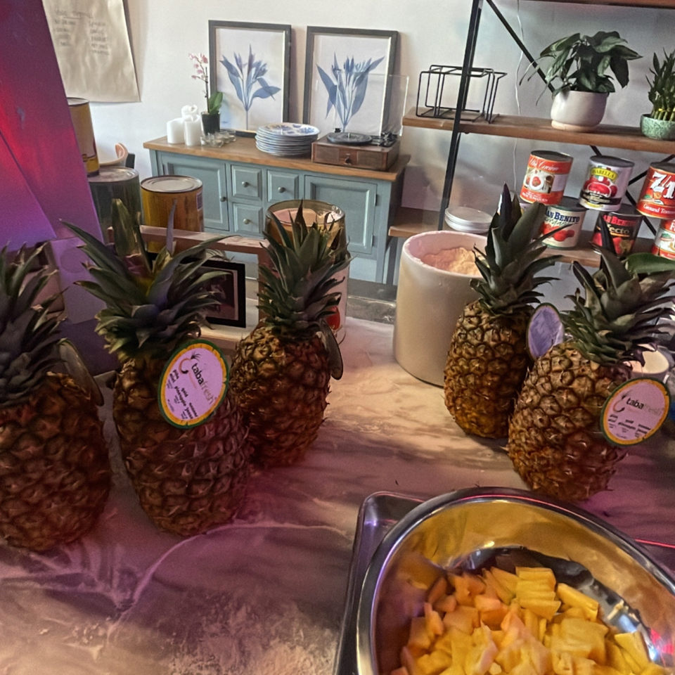 Whole pineapples and a bowl of diced pineapple on a counter with pizzeria decor in the background.
