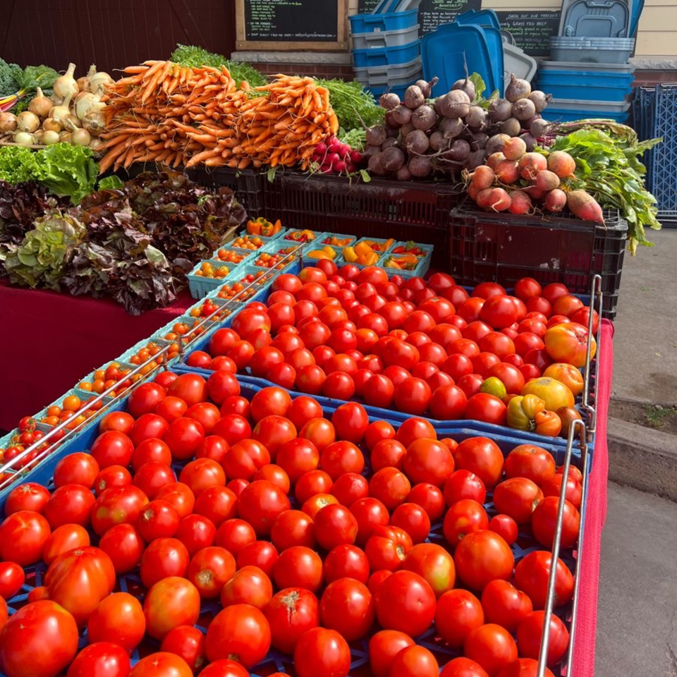 Fresh produce stand with vibrant red tomatoes, carrots, onions, and leafy greens.