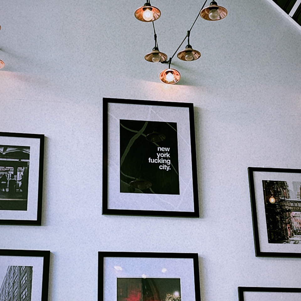 A white wall adorned with framed black and white pictures and industrial hanging lights.
