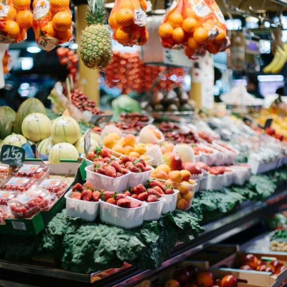 A vibrant market stall displays fresh produce, including strawberries, melons, oranges, and pineapples.