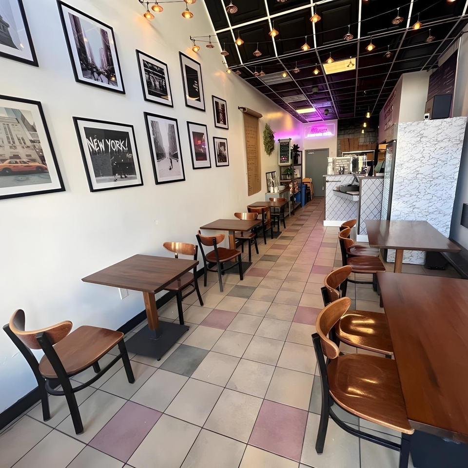 Interior of Bloom pizzeria with New York-themed art, wooden tables and chairs, and a counter area.